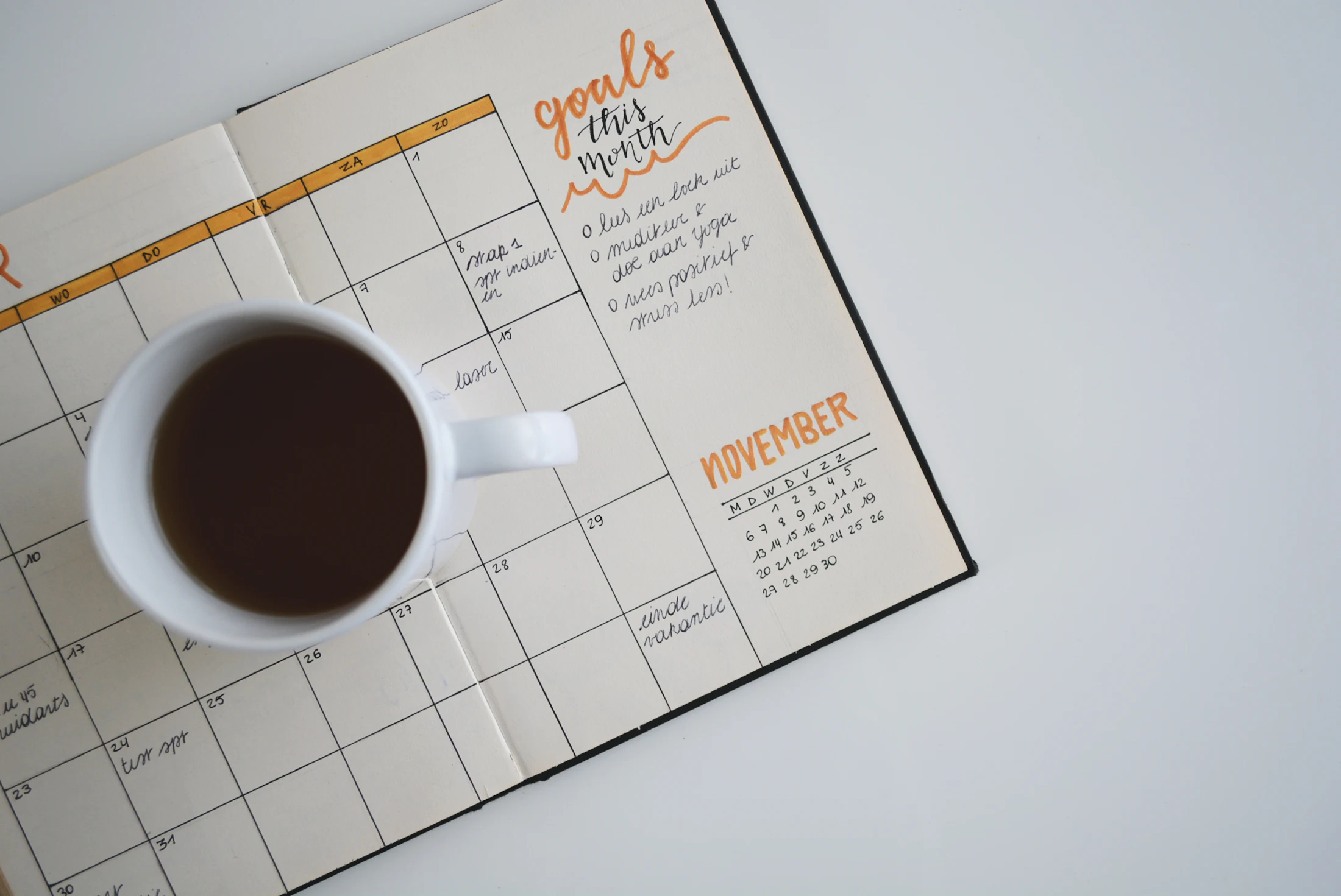 Agenda mensal aberta ao lado de uma xícara de café